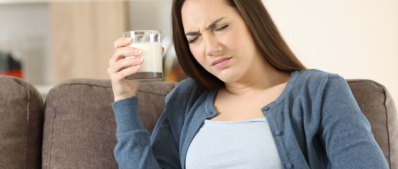 Kvinne sitter i sofa med et glass melk og ser ut til å ha ubehag.