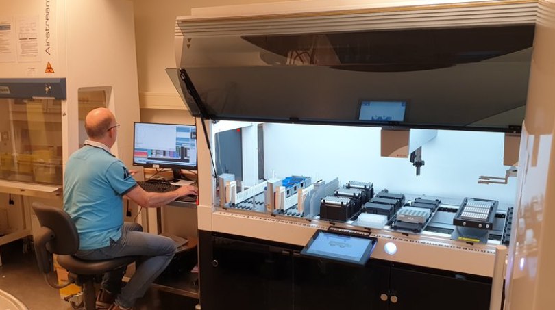 En mann som arbeider ved en datamaskin ved siden av en stor laboratorierobot.