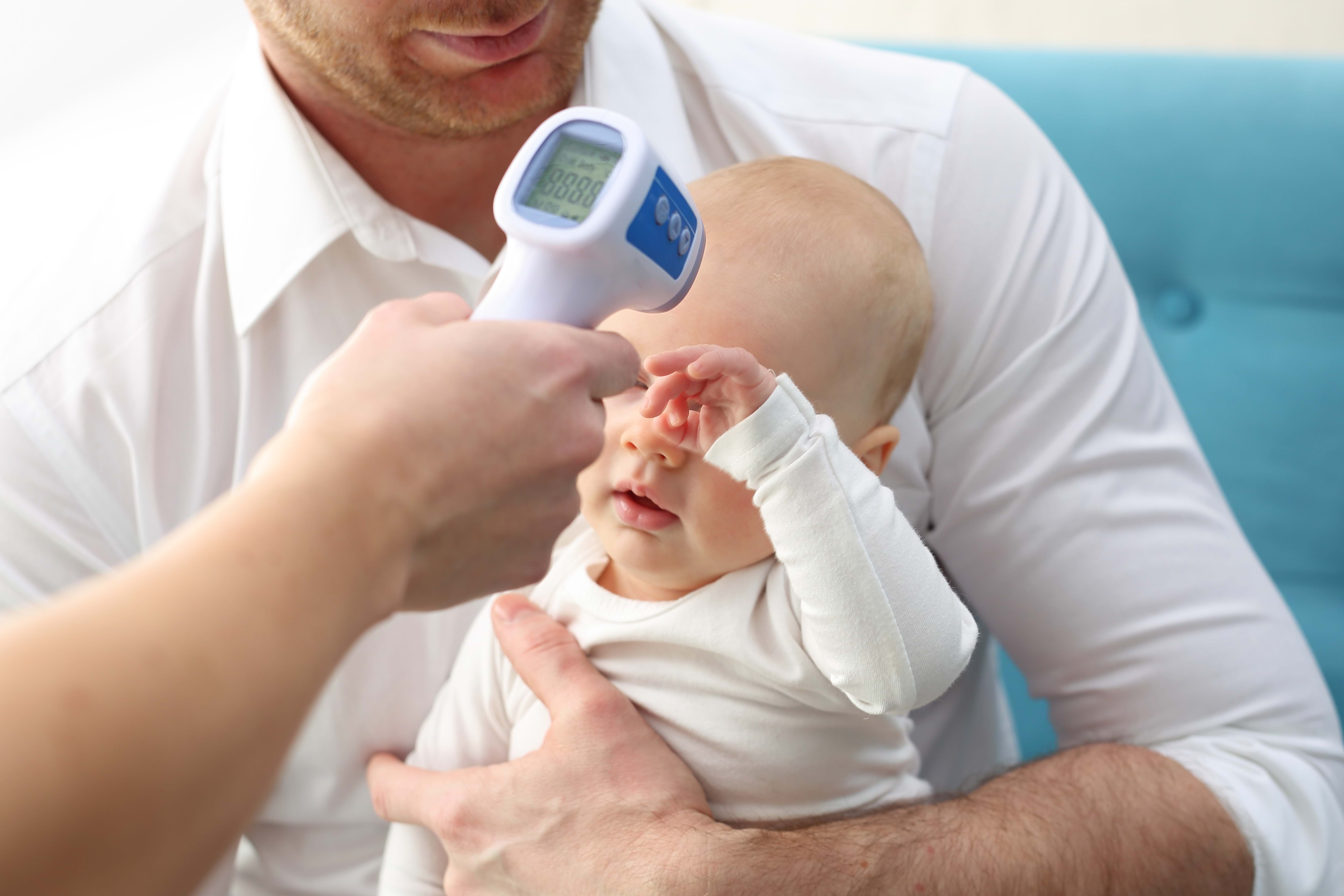 Baby på fars fang, helsepersonell måler feberen med digital termometer