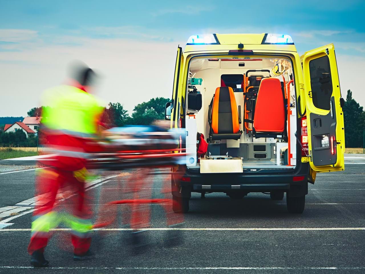 Ambulansepersonell i bevegelse mens de frakter en pasient på båre mot en åpen ambulanse.